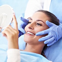 young woman admiring her own smile after seeing cosmetic dentist in Astoria 