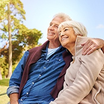 happy elderly couple sitting on a park bench 