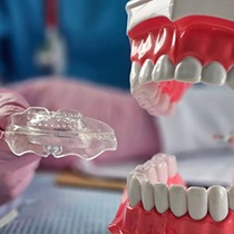 Close up of dentist holding a nightguard with a dental model nearby