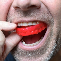 man putting a red mouthguard into his mouth