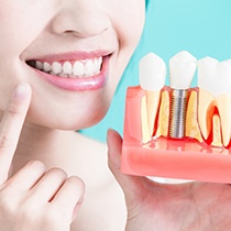 Woman pointing to mouth holding model of dental implants in Astoria.