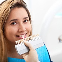 cosmetic dentist in Astoria holding a row of veneers up to a patient’s smile 