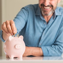 man putting coins into a pink piggy bank 