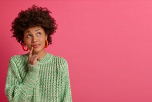 Woman in a green sweater with her finger to her lip as she thinks