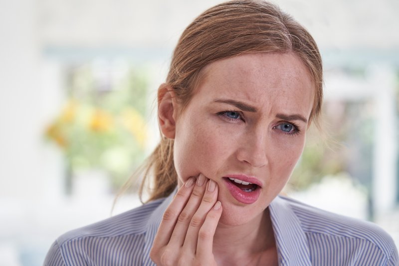 Woman with dental implants rubbing her jaw in concern