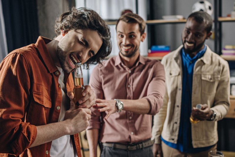 person opening a bottle with their teeth as friends watch