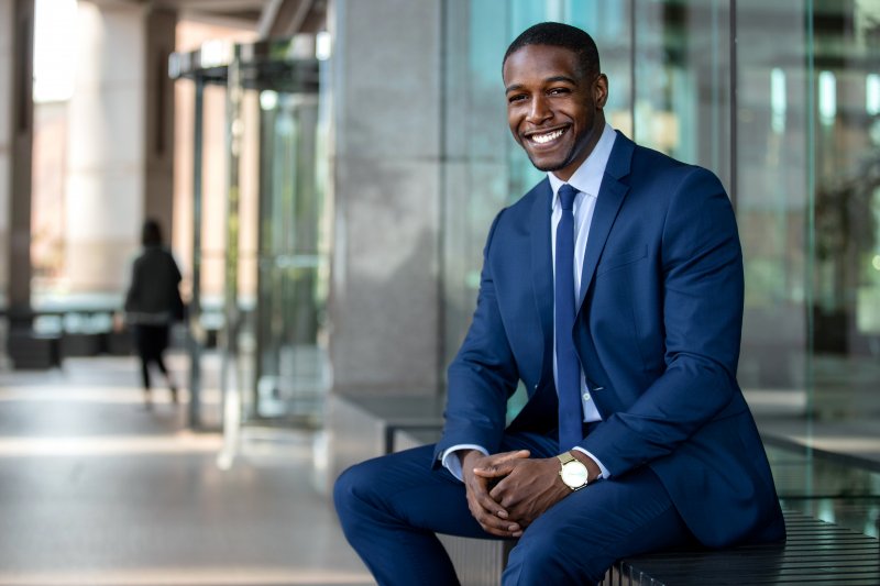 A young professional smiling outside of an office building.