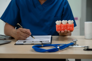 Dentist sitting at his desk and holding an oversized model of three teeth