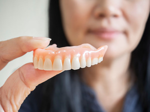 Woman holding a full denture between her finger and thumb